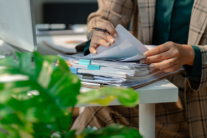 A person sits at their desk and files through paperwork.