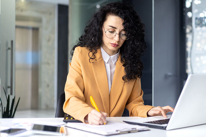 A young woman sits at her desk and works on her laptop.