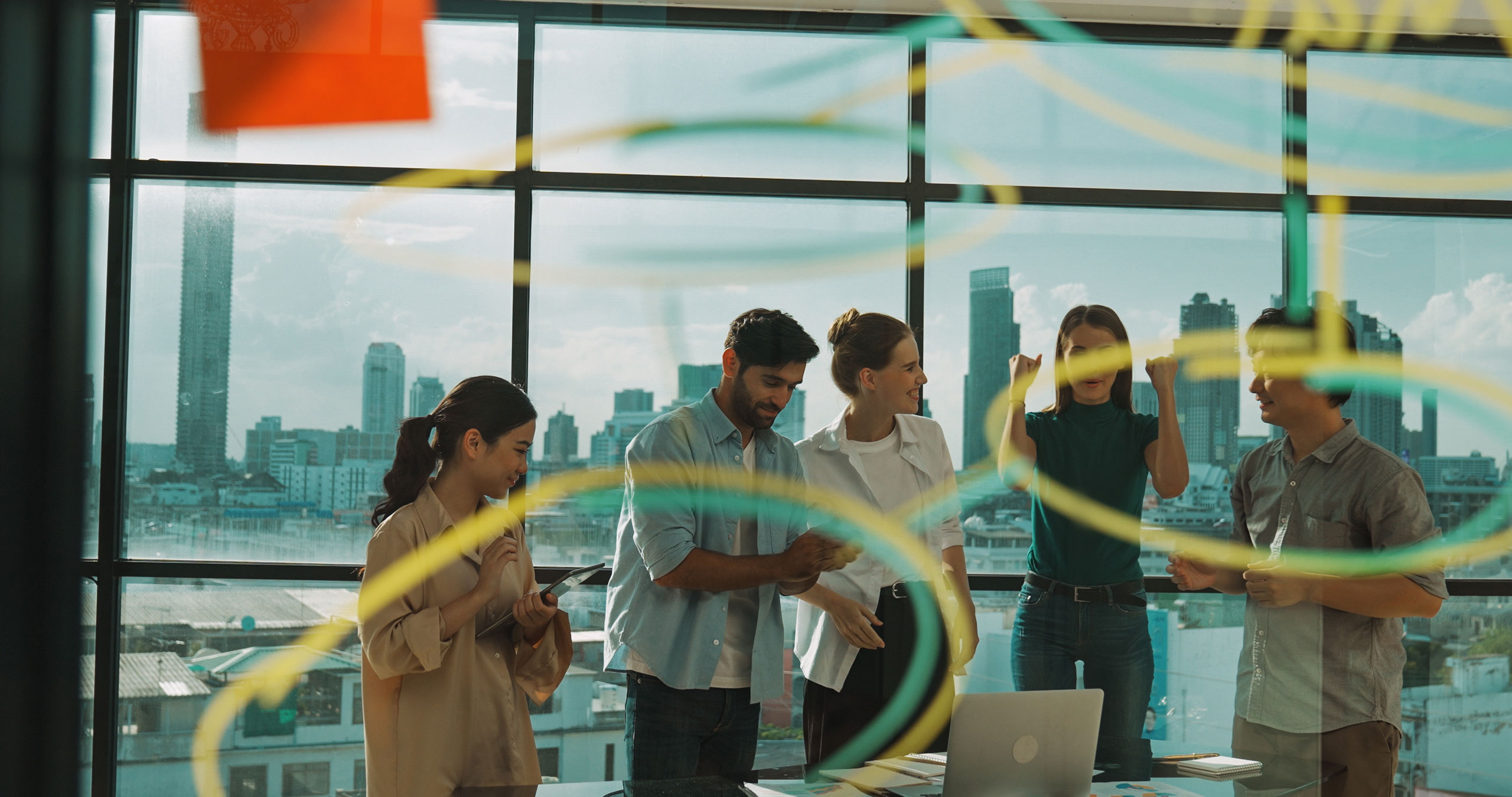 A team of employees gathers together in another room, as you look through a glass divider.