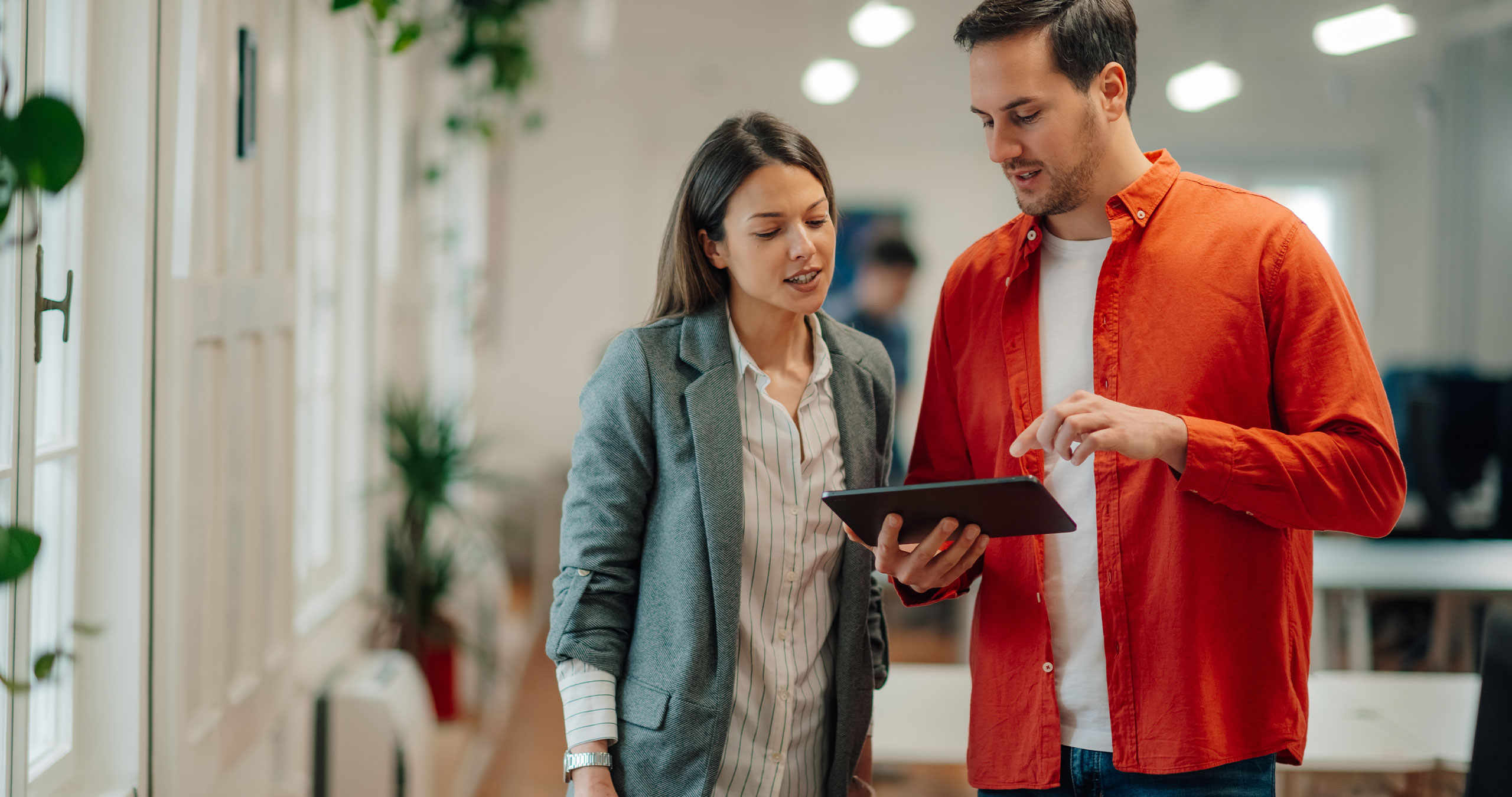 Two co-workers talk to one another while looking at a tablet.
