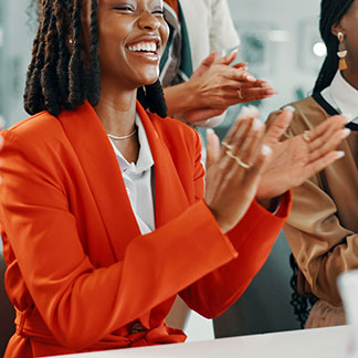 A group of women, gathered in the office, applause one another.
